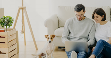 גבר ואישה מסתכלים על מחשב נייד ולצידם כלב