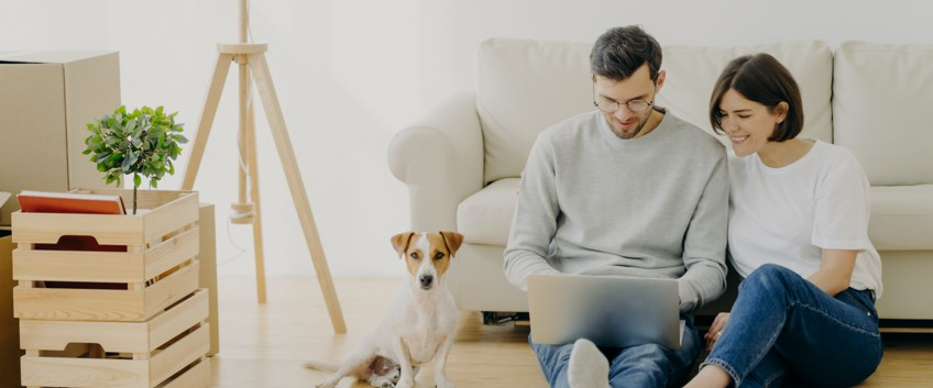 גבר ואישה מסתכלים על מחשב נייד ולצידם כלב